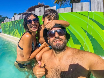 Happy family of threebearded dad in sunglasses and hat, mom in a bikini and their childtaking a