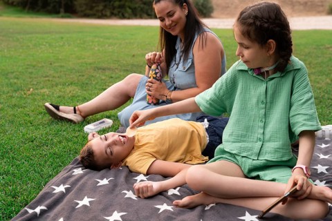 A family shares a joyful moment on a grassy picnic, with a disabled girl using a tracheostomy and a