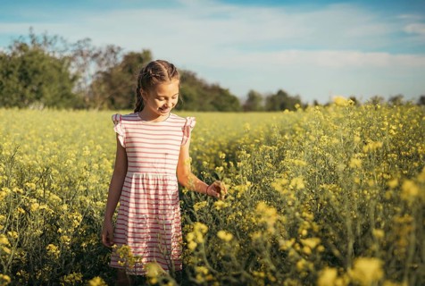 A young girl in a striped dress enjoys a peaceful moment in a blooming yellow flower field. She