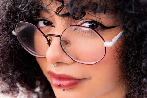 Close-up of a stylish latin woman with large glasses, curly hair, and facial piercings, showcasing