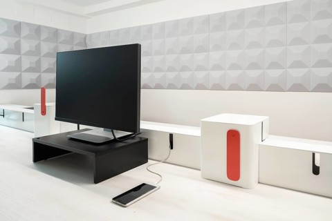 A modern office setup featuring a sleek monitor on a black stand, a smartphone charging via a white