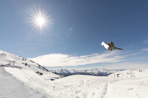 A snowboarder performing an aerial trick against the crisp, clear blue sky, with snowy mountain