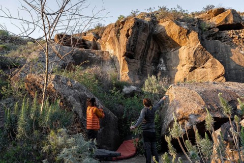 Enthusiasts tackle a rugged boulder surrounded by lush vegetation, capturing the natural drama and