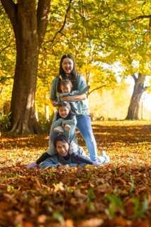 Asian family of four delights in a playful autumn day outdoors, surrounded by colorful falling