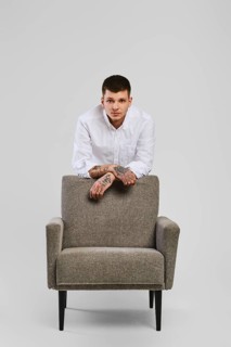 Full length studio portrait of young barefoot man in white shirt and ivory trousers leaning to