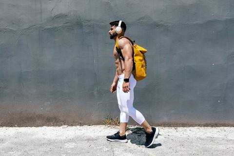Fit man walking along a concrete path, wearing white leggings and black sneakers. He carries a