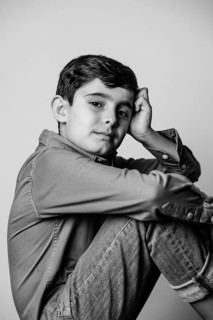 A young boy in casual attire sits pensively, resting his head on his hand. The monochrome image