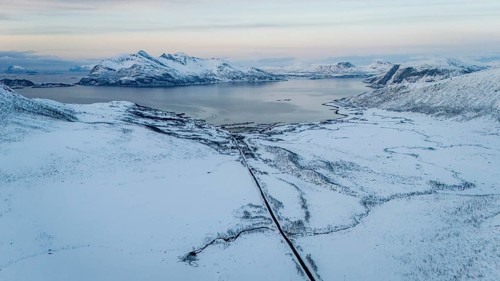 Breathtaking aerial image of a snowy coastal region in Norway, with vast white plains, mountain