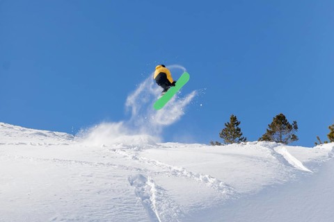 A snowboarder in a yellow jacket and green snowboard catches air on a snowy slope against a