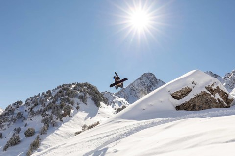 A snowboarder performs an impressive jump against a clear blue sky, surrounded by snow-covered
