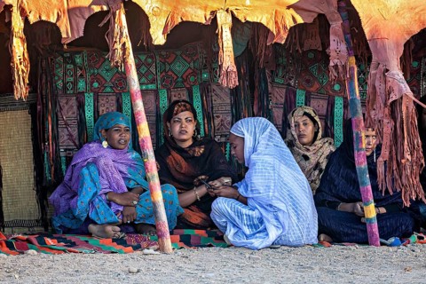 Women sit in a tent and talk to each other, surrounded by colourful fabrics, Veiled woman at the