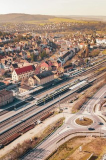 Aerial view of a city with railroad tracks and an intersection under bright sunlight, Mühlacker,