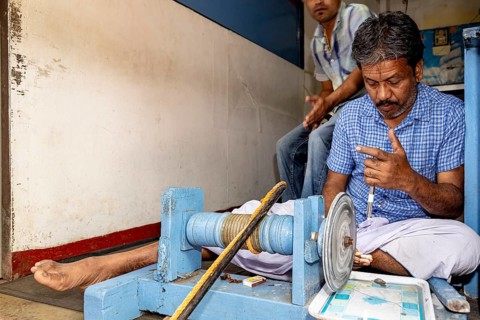 A seated man works on a machine, shows finger positions and is concentrated, the gemstone cutters