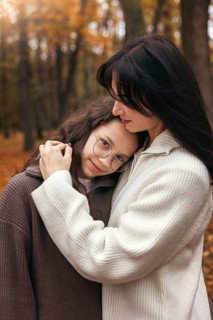 A comforting embrace between a mother and daughter in an autumn forest. The warmth of their