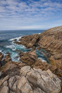 Rocky west coast of the Quiberon peninsula in Brittany, France, with a partly cloudy sky. Crashing