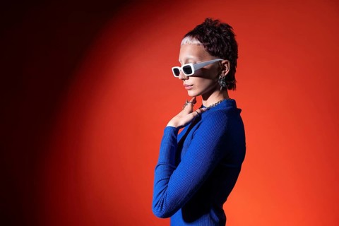 A fashionable young woman in a vibrant blue top poses confidently against a bold red background.