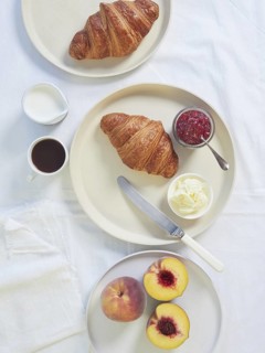 Continental breakfast served on white tablecloth croissants, butter, jam, cup of coffee and fresh