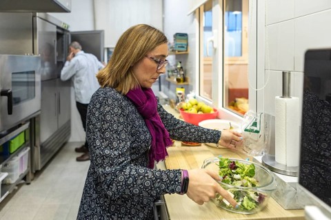 A woman prepares a fresh salad in a modern kitchen, using a glass bowl. Your partner can be seen in