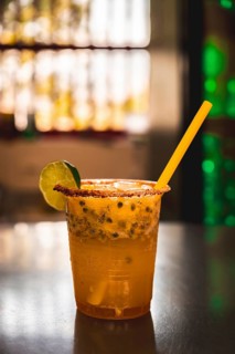 A refreshing Colombian michelada served in a plastic cup, featuring passion fruit, lime, and a