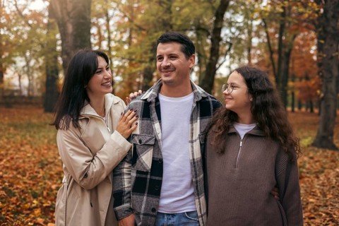 A cheerful family walks together in a park surrounded by vibrant autumn leaves. Their smiles