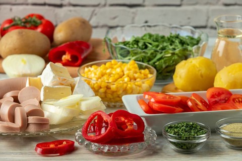 Preparation for salad with potatoes, tomatoes, peppers, sausage, corn, onions, cheese and arugula