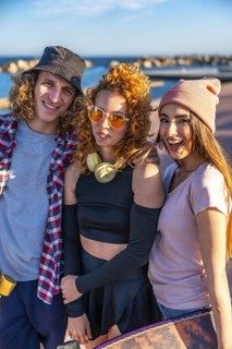 Diverse group of millennials spending time together outdoors at a coastal location during sunset.
