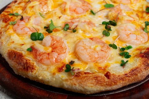 Four cheese pizza with shrimp and fresh microgreens, served on a wooden board, homemade, no people