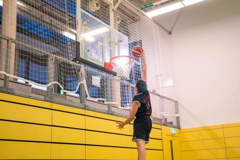 A player energetically places the ball in the basket in a yellow gym, basketball TSV Calw, Germany