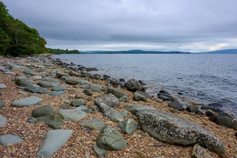 Rocky coast with trees on horizon under cloudy sky, Tarbert, Loch Fyne, Scotland, United Kingdom,