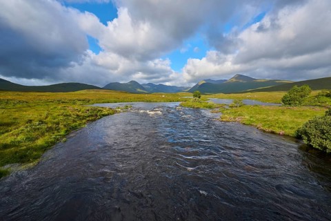 River flows through green landscape under sky with clouds, Rannoch Moor, Bridge of Orchy, Scotland,