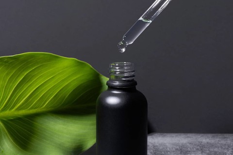 A dropper releases a clear, viscous liquid into an elegant black matte cosmetic bottle, set against