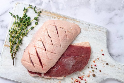 Fresh raw duck breasts, spread on a wooden cutting board, with herbs and spices, on a white marble