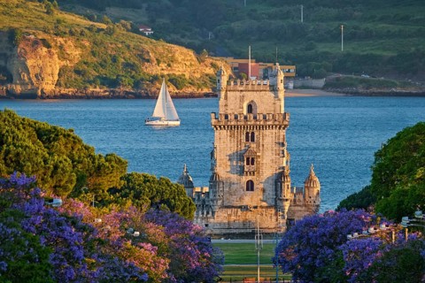 Belem Tower stands majestic against the Tagus River, surrounded by blooming jacaranda trees and