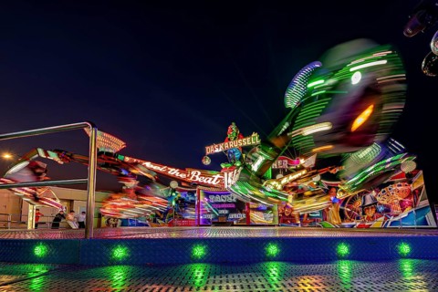 An illuminated carousel at a fair at night showing sparkling lights in rapid motion, carousel and