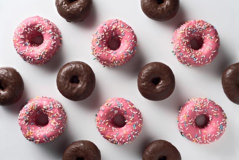 Top view of an arrangement of pink strawberry and dark chocolate donuts, each topped with colorful