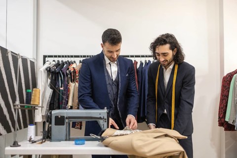 Tailor in a suit store work on fabric with precision, surrounded by clothing and sewing tools,