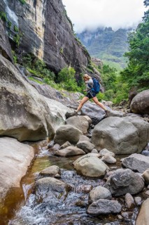 Female hiker jumping over rocks, Tugela Gorge or Tugela Gorge in the riverbed, Drakensberg National