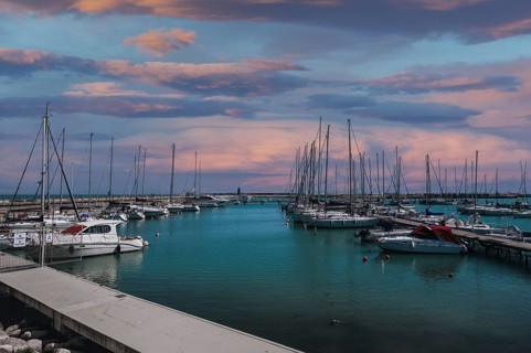A stunning marina under a vibrant sunset sky in Civitanova Marche, Italy. The scene captures the