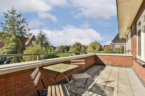 A charming outdoor terrace featuring simple wooden furniture, surrounded by quaint homes and lush