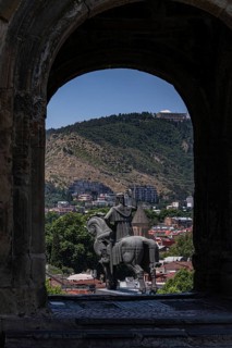 An equestrian statue framed by an archway overlooks Tbilisi's blend of historical and modern