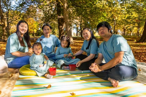 An Asian family enjoys a picnic during autumn, surrounded by vibrant foliage. They sit on a