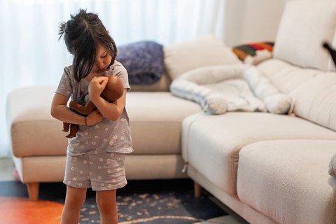 A young girl lovingly embraces her doll in a cozy living room, capturing a tender moment. The scene