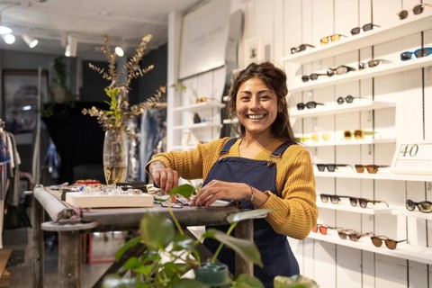 A friendly store assistant smiles warmly while preparing accessories in a modern sunglasses store