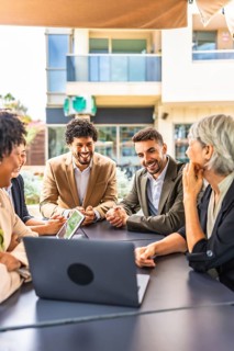 Vertical photo of a group of diverse business people using laptop during a meeting in a cafeteria