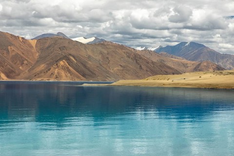 The serene Pangong Tso lake in Ladakh, surrounded by majestic Himalayan mountains, reflects clear