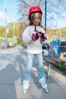 A young girl wearing a protective helmet and gloves is preparing to skate by putting on her roller