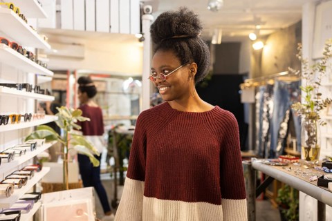 A young woman in a stylish sweater smiles while trying on trendy sunglasses in a fashionable store.