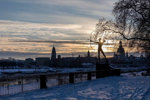 Bronze figure The archer in the snow, in the background the Elbe with drift ice and the old town