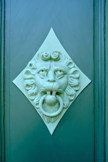 Old historical door knocker with lion's face on the coffered panel of a green door leaf