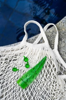 Top view of a green aloe vera gel tube and spherical green capsules placed on a white mesh bag